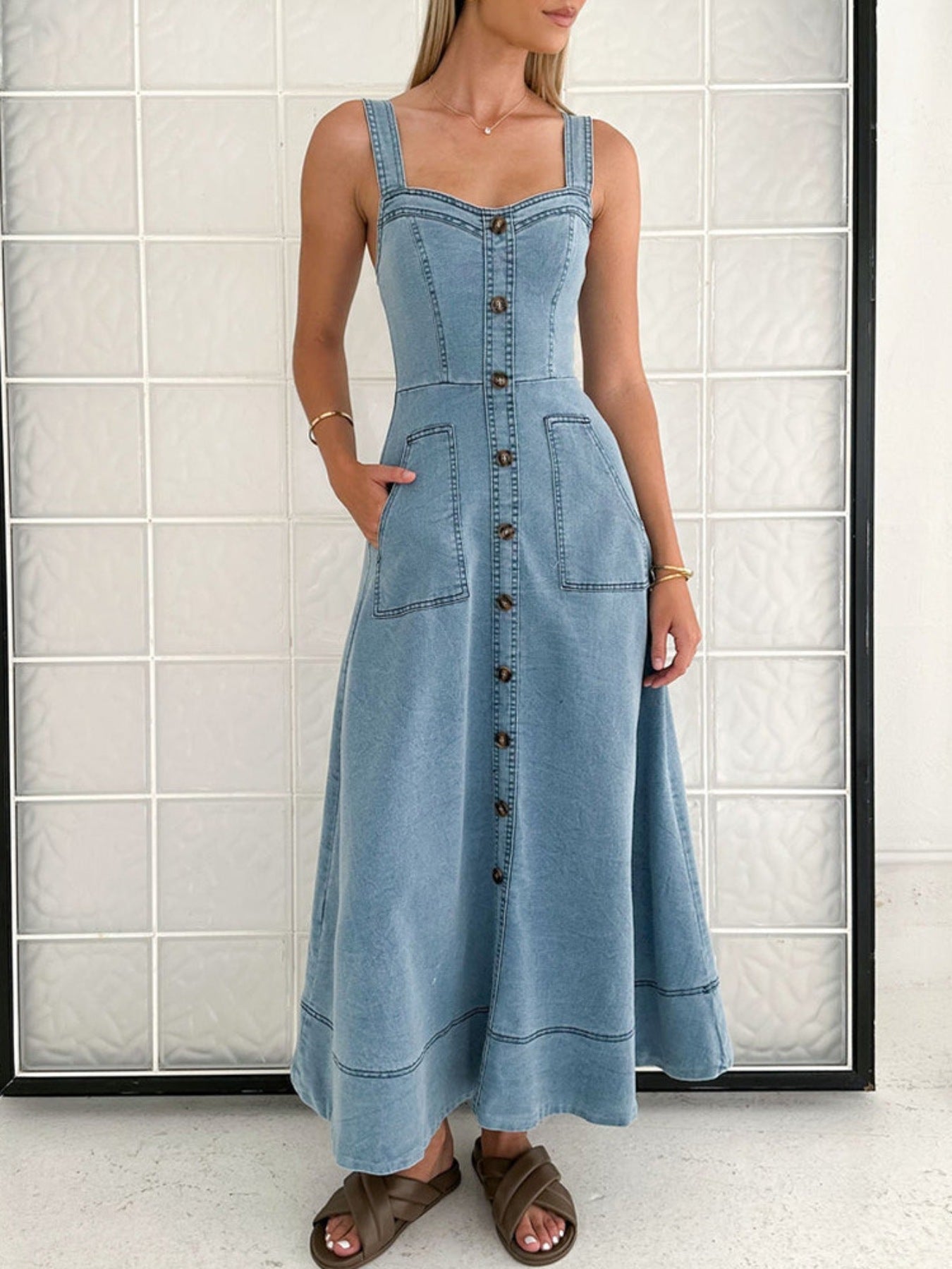 Model trägt ein langes A -Linien Jeanskleid mit Knopfleiste und breite Träger kombiniert mit Sandalen 