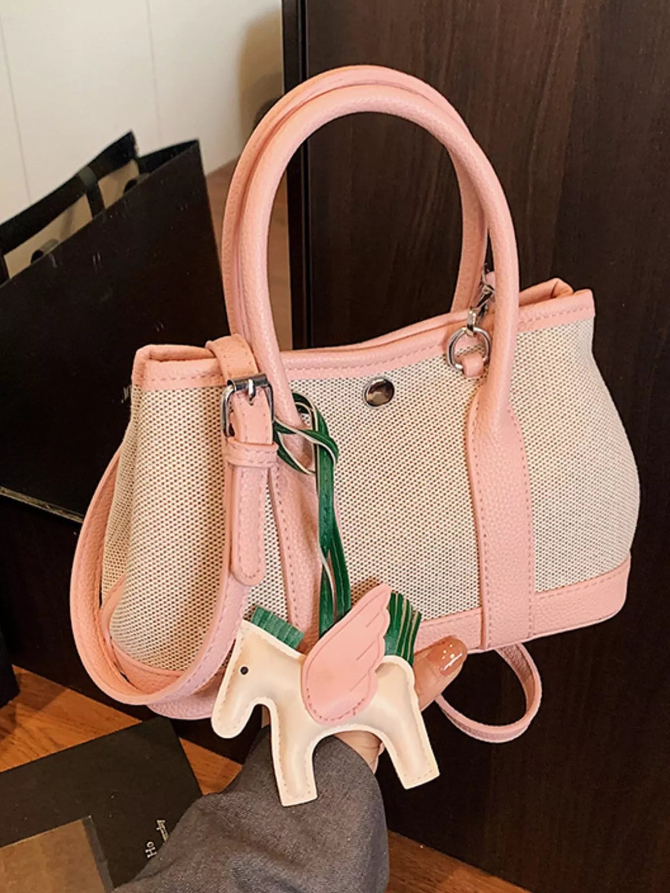 Kleine Handtasche aus beigem Stoff mit rosafarbenen Griffen und Rand, verziert mit einem dekorativen Pferdeanhänger