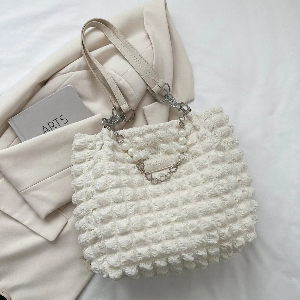 Weiße Handtasche mit strukturierter Oberfläche, kurzen Trägern und dekorativer Kette mit Perlen.