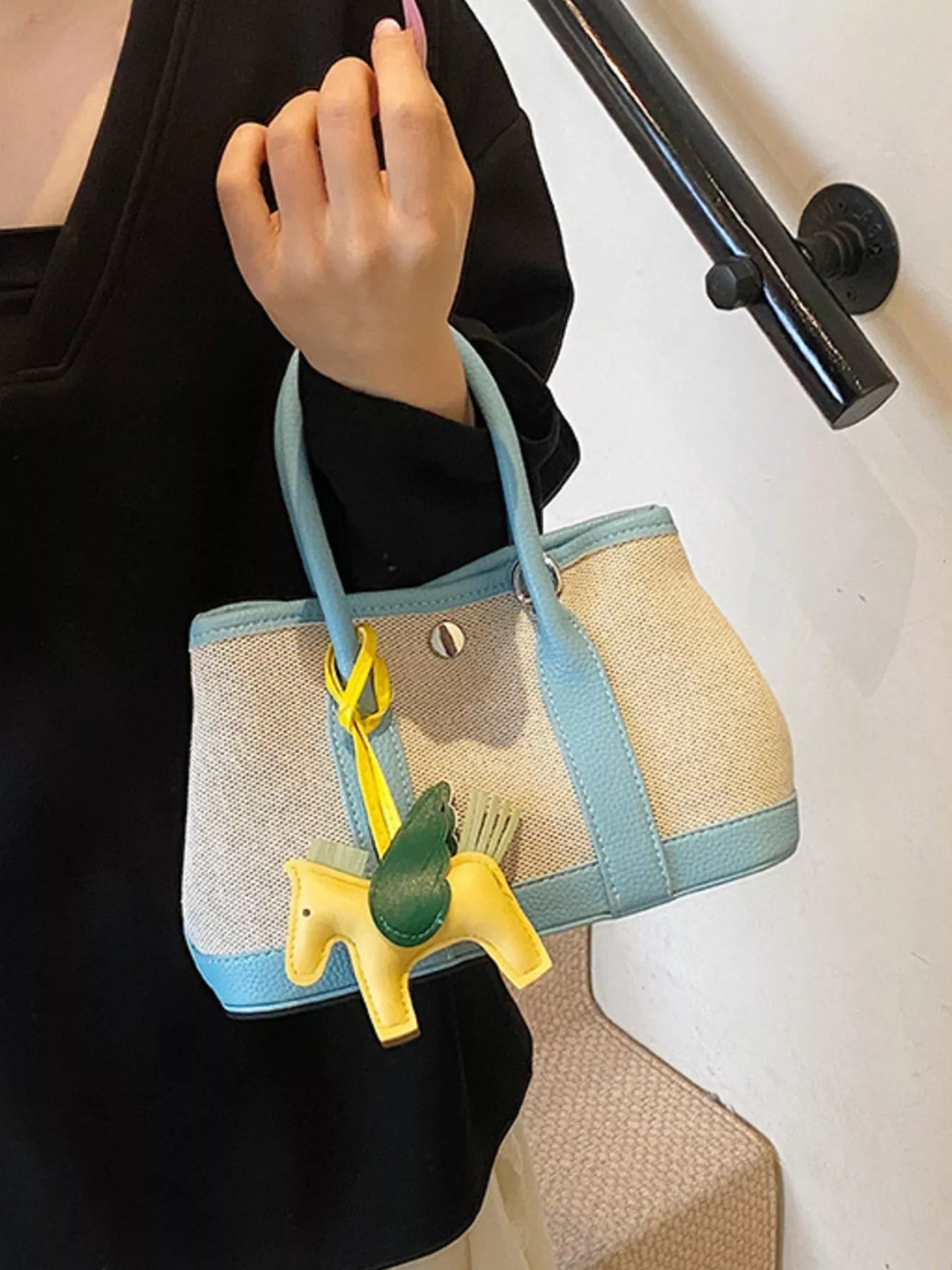 Kleine Handtasche aus beigem Stoff mit hellblauen Griffen und Rand, verziert mit einem gelben Pferdeanhänger