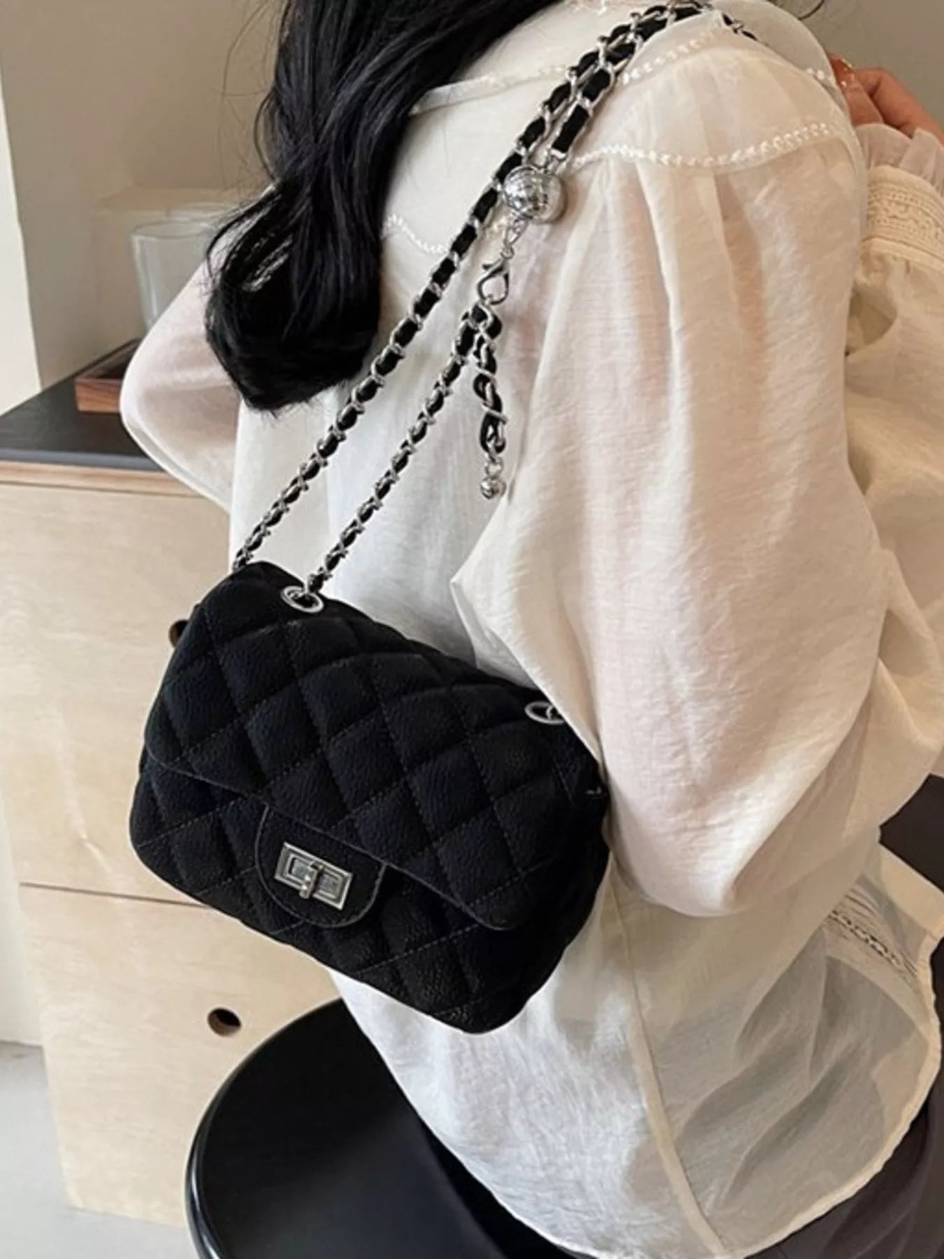 Schwarze gesteppte Schultertasche mit Kettenriemen, getragen über einer weißen Bluse. 👜