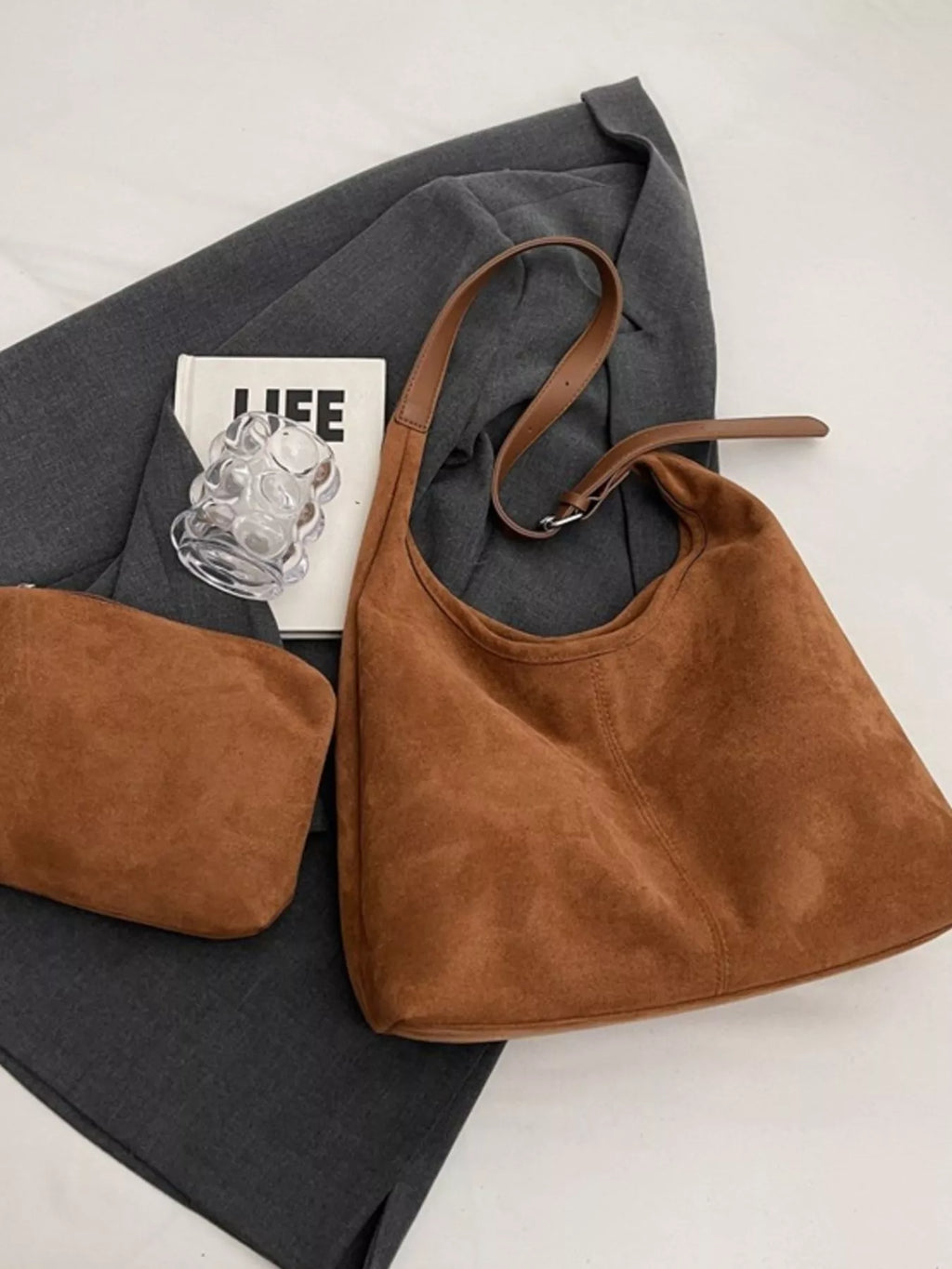 Selina - Wildlederoptik-Tasche in braun, stilvoll kombiniert mit einem grauen Blazer und einem Buch sowie einer kleinen Tasche.
