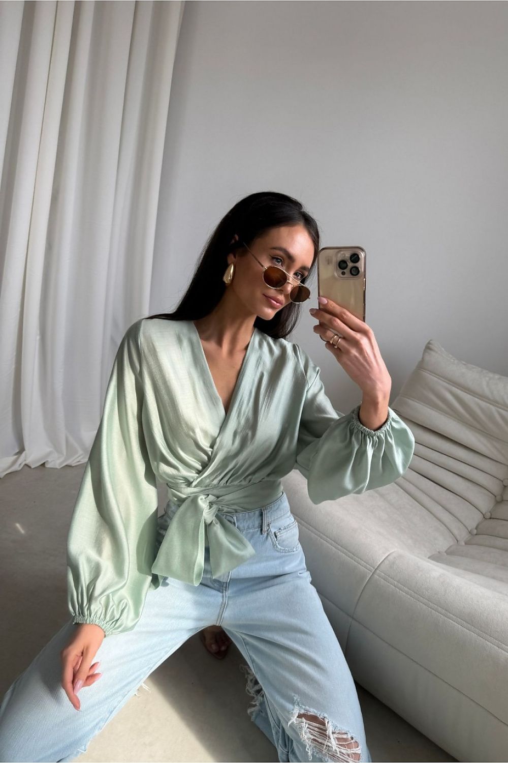 Elegante Wickelbluse aus glänzendem Satin in Pastellgrün mit Puffärmeln und Bindegürtel, getragen von einem Model mit heller Jeans.