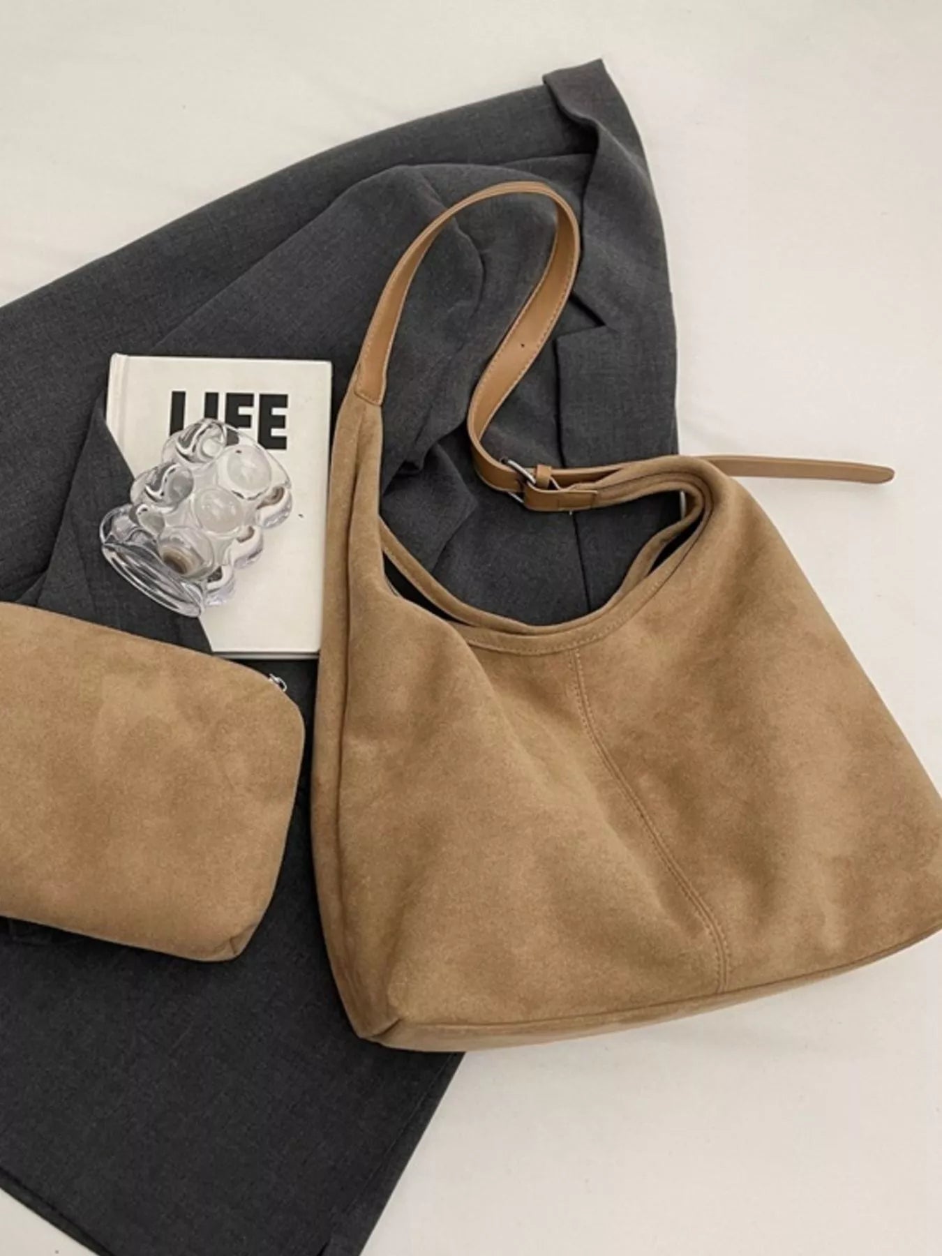 Selina - Wildlederoptik-Tasche in tan, kombiniert mit einer grauen Jacke und einem Buch auf einem hellen Untergrund.
