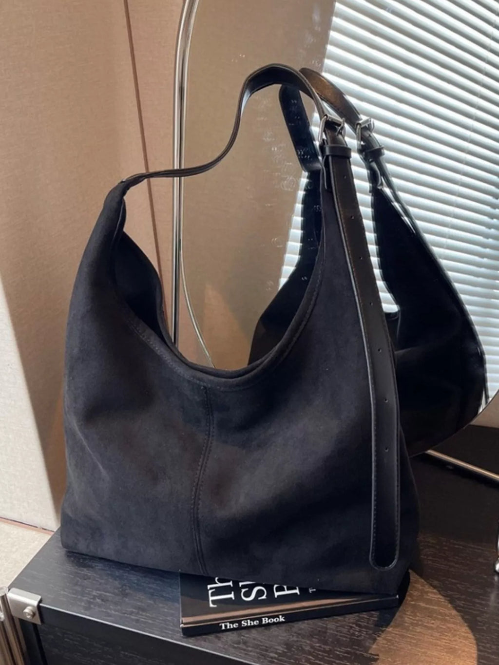 Selina - Wildlederoptik-Tasche in Schwarz auf einem Tisch mit einem Spiegel im Hintergrund.